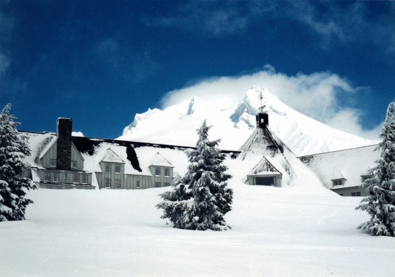 Snow-covered mountain lodge surrounded by pine trees in a winter wonderland.